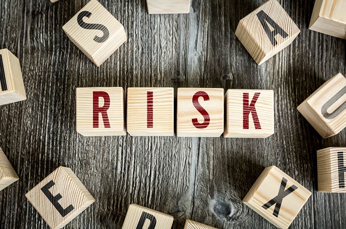 Photo en plongée de cubes en bois posés sur une surface en bois foncé, formant au centre le mot RISK en lettres rouges, entourés de cubes avec d'autres lettres noires.