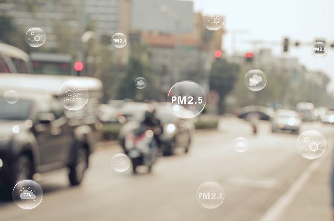 Vue floue d’une rue de ville avec voitures et moto en circulation, survolée de bulles semi-transparentes affichant les mentions “PM2.5”, “CO2” et des icônes de pollution atmosphérique.