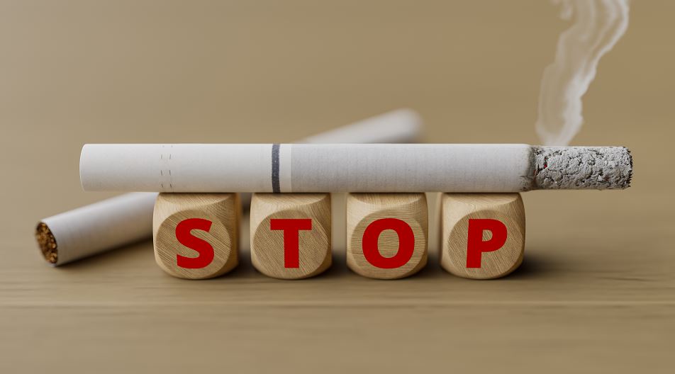 Gros plan d’une cigarette allumée reposant sur quatre cubes en bois gravés des lettres S-T-O-P, symbolisant l’appel à l’arrêt du tabac
